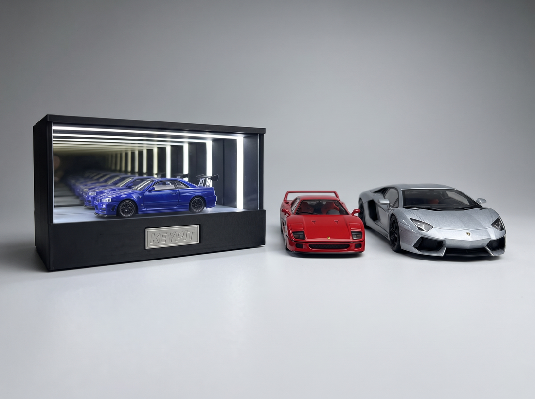 A 1:64 diecast in the lit KP Design Infinity Garage next to a larger 1:43 and an even larger 1:18 model car showing scale differences