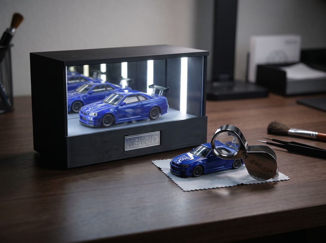 A loose 1:64 diecast car being examined with a jeweler's loupe beside a lit KP Design Infinity Garage