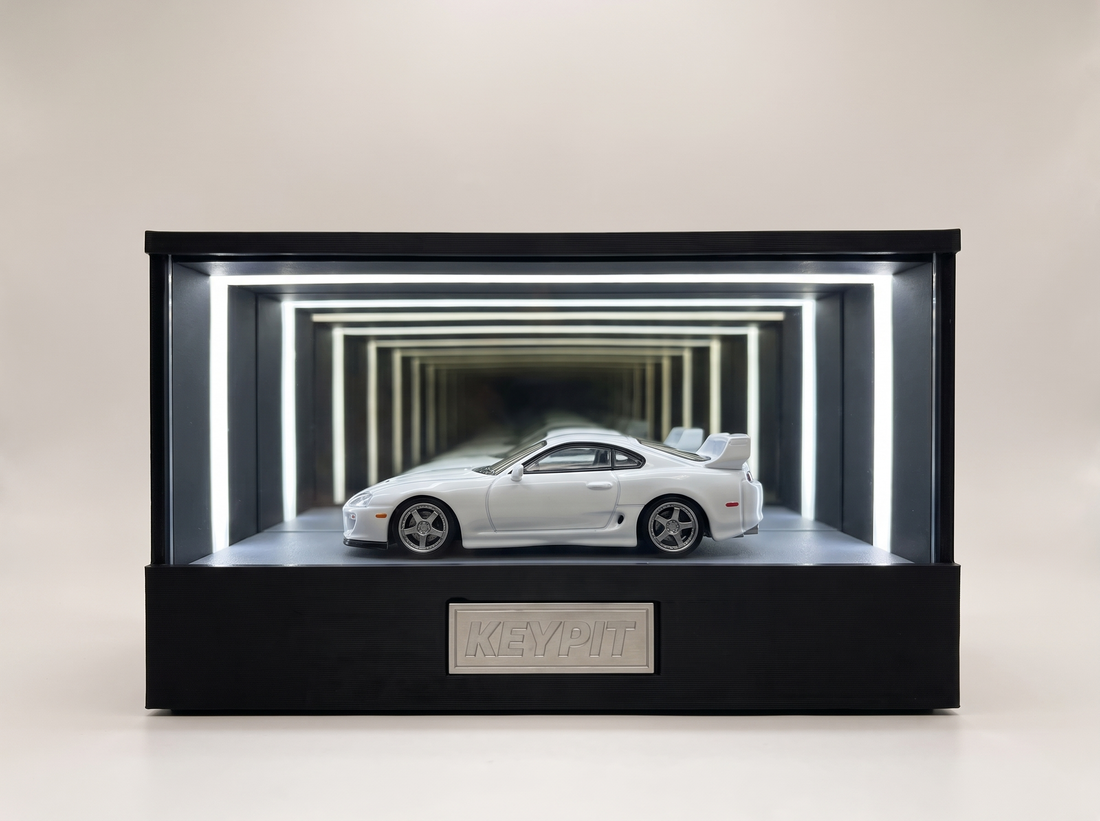 A white Toyota Supra A80 Mk4 1:64 diecast with rear wing displayed in the lit KP Design Infinity Garage case