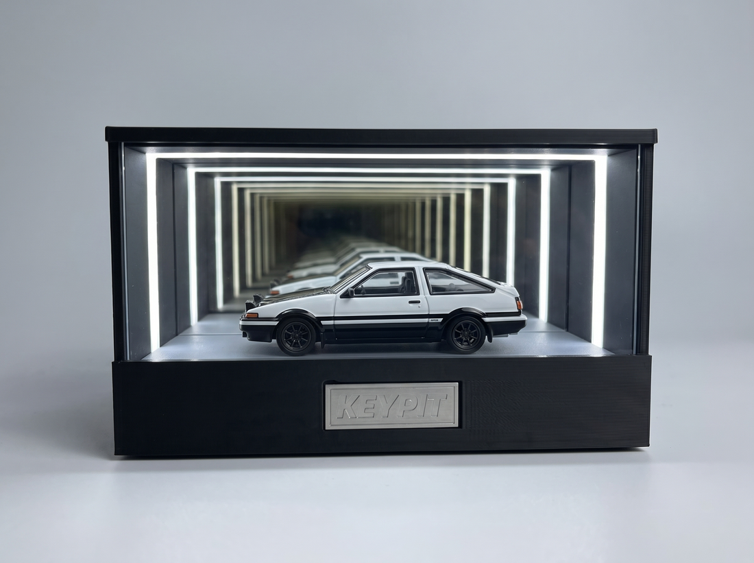 A black-and-white panda Toyota AE86 Trueno 1:64 diecast displayed in the lit KP Design Infinity Garage case