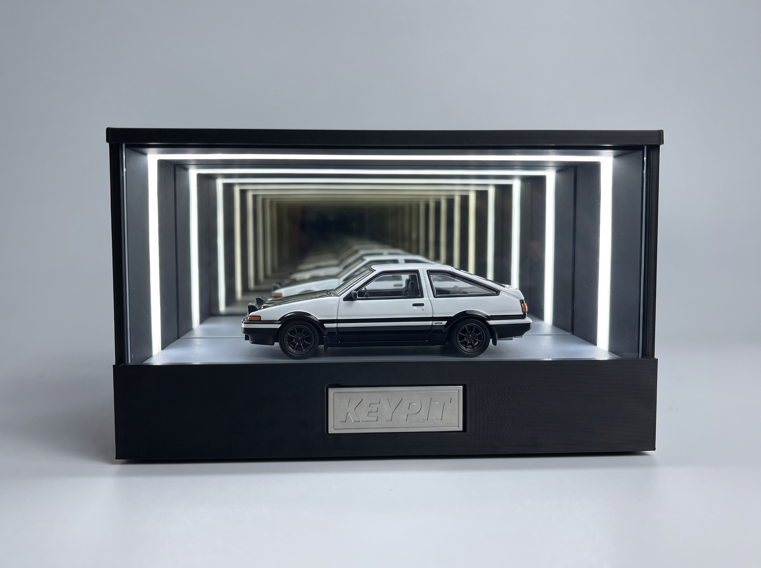 A black-and-white panda Toyota AE86 Trueno 1:64 diecast displayed in the lit KP Design Infinity Garage case
