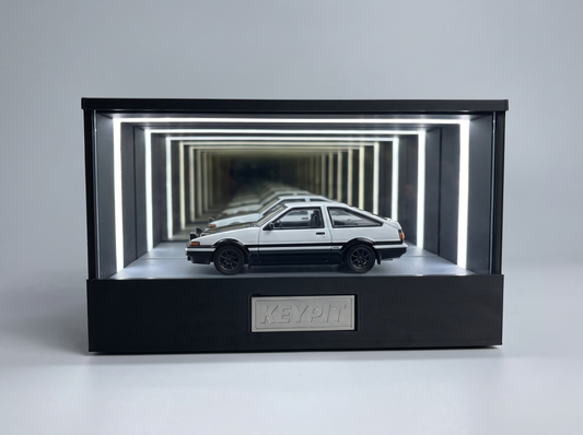 A black-and-white panda Toyota AE86 Trueno 1:64 diecast displayed in the lit KP Design Infinity Garage case