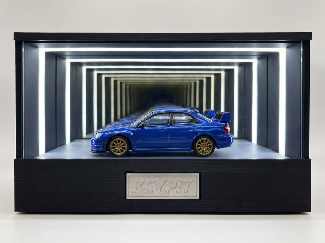 A blue Subaru WRX STI 1:64 diecast with gold wheels and rear wing displayed in the lit KP Design Infinity Garage case