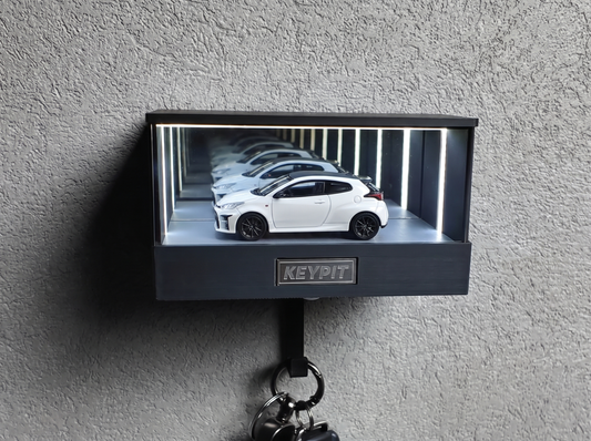 A white 1:64 Toyota GR Yaris shown in side profile inside a wall-mounted KP Design Infinity Garage display case