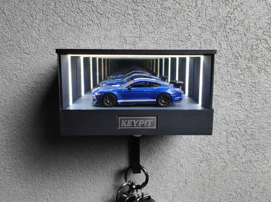 A blue 1:64 Ford Mustang Shelby GT500 with white stripes shown in side profile inside a wall-mounted KP Design Infinity Garage display case