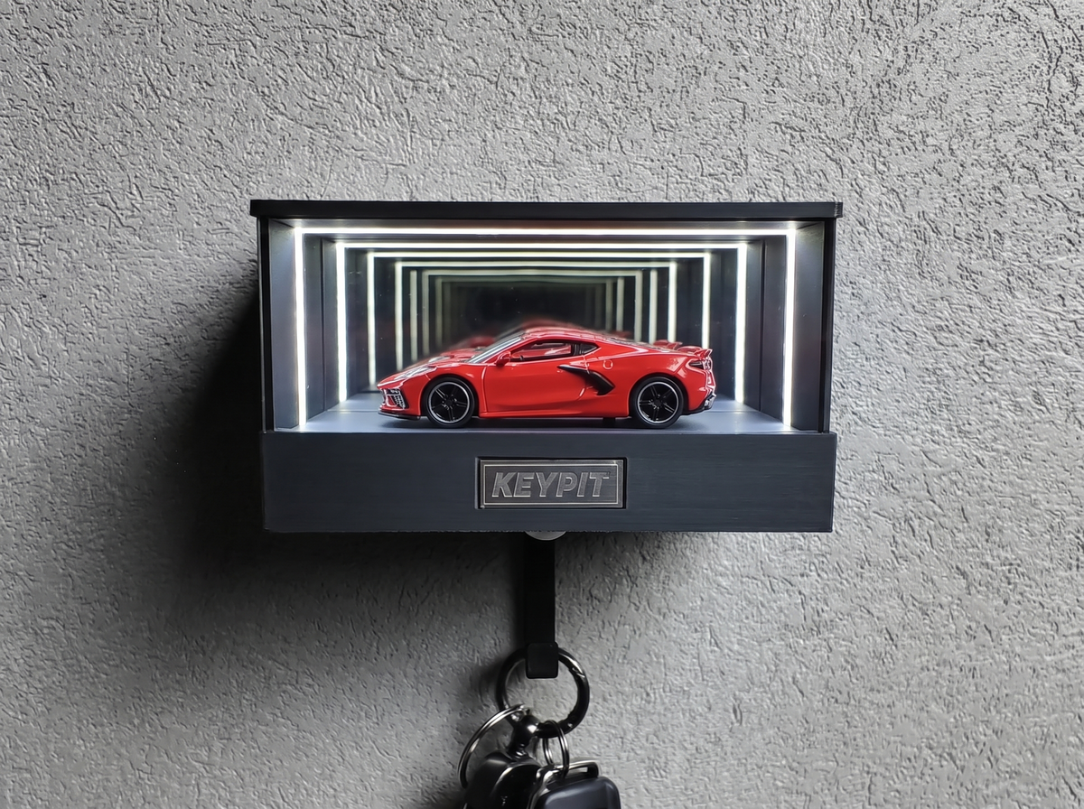 A red 1:64 Chevrolet Corvette C8 shown in side profile inside a wall-mounted KP Design Infinity Garage display case