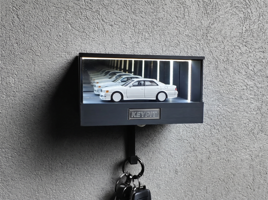 A white 1:64 Toyota Chaser JZX100 shown in side profile inside a wall-mounted KP Design Infinity Garage display case