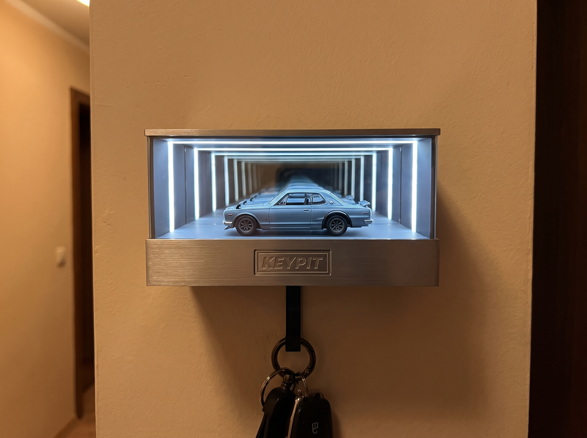 A lit wall-mounted infinity-mirror display case holding a single 1:64 diecast car in a home hallway