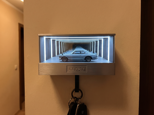 A lit wall-mounted infinity-mirror display case holding a single 1:64 diecast car in a home hallway