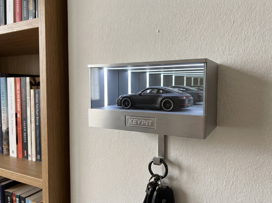 A lit wall-mounted display case holding a single 1:64 diecast car on a living room wall beside a bookshelf