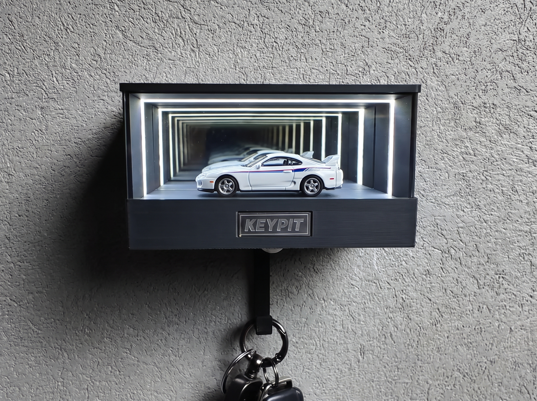 A white 1990s Japanese sports coupe in 1:64 scale, lit inside a wall-mounted display case with a key hook underneath