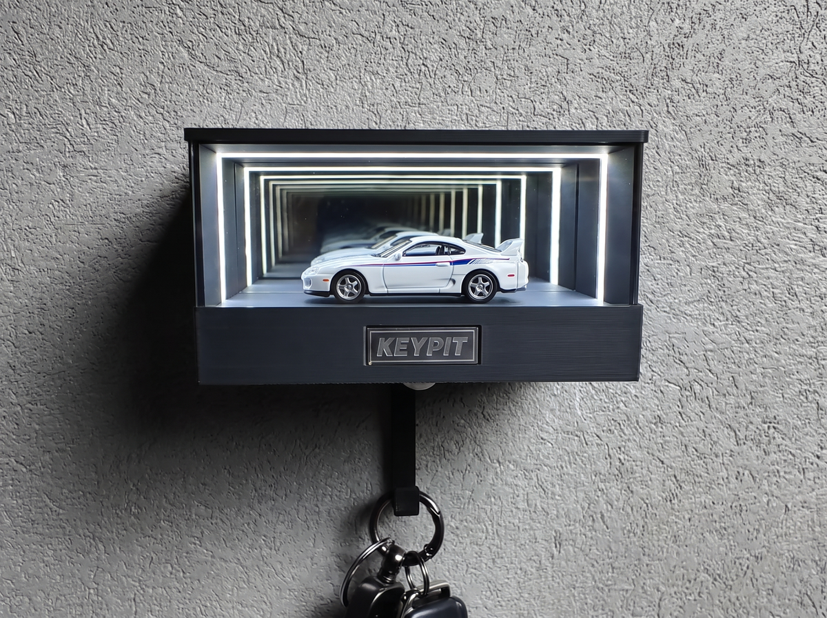 A white 1990s Japanese sports coupe in 1:64 scale, lit inside a wall-mounted display case with a key hook underneath