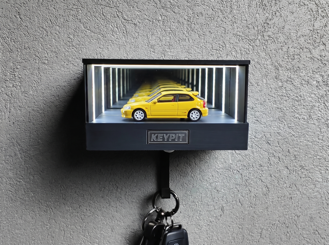 A yellow 1:64 hot hatch lit inside a wall-mounted display case with a key hook underneath
