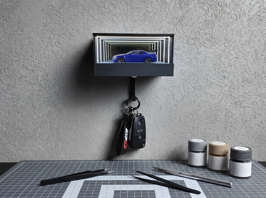 A lit wall-mounted display case above a work surface with tools and a cutting mat